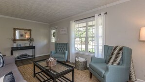 A living room with a sofa, armchair, coffee table, and a console table with decorative items. - 4BR Ranch • 1 Mile to Downtown Cartersville (Cartersville)