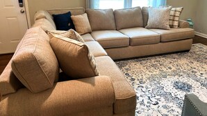 Ein beiges Ecksofa mit mehreren Kissen, einem gemusterten Teppich und einer Tür mit Zahlenschloss.