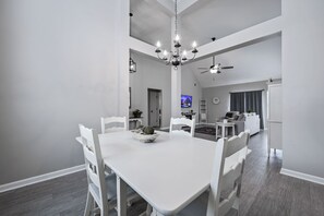 A spacious dining area with a white table and chairs, a chandelier, and a ceiling fan.