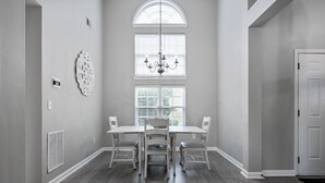 Un coin repas comprenant une grande table et quatre chaises, un lustre et une fenêtre avec des stores.