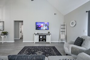A modern living room with a flat-screen TV mounted on the wall, a white console table with decorative items, a grey sofa, and a patterned rug.