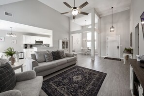 A spacious living room with a grey sofa, a dark patterned rug, and a ceiling fan.