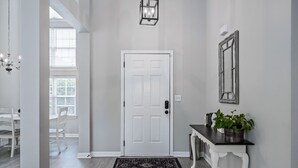 Un couloir avec une porte blanche, une petite console sur laquelle est posée une plante, et un tapis noir.