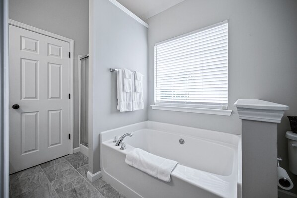 A bathroom with a white bathtub, a door, and a window with blinds.