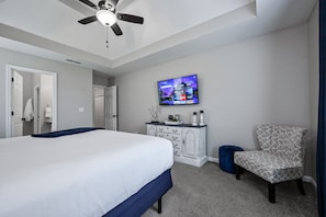 A bedroom with a bed, a ceiling fan, a TV mounted on the wall, a dresser, a chair, and a blue bean bag.