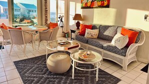 Una sala de estar acogedora con muebles de mimbre, una mesa de centro de vidrio y un cuadro colorido sobre el sofá.