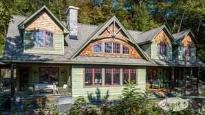 Une grande maison à deux étages, à l’extérieur vert et dotée de nombreuses fenêtres, entourée d’un jardin bien entretenu.