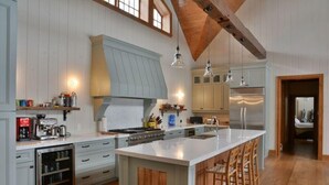Une cuisine spacieuse dotée d’un grand îlot central, de poutres apparentes en bois et d’un réfrigérateur moderne en acier inoxydable.