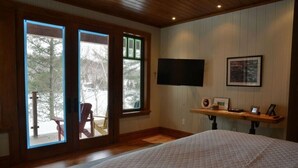 Une chambre avec un grand lit, un téléviseur fixé au mur et une fenêtre donnant sur une terrasse.