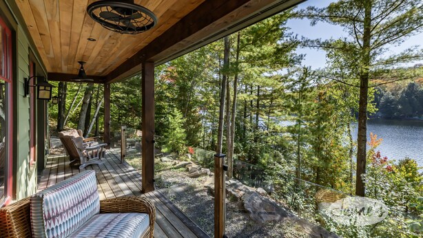 Une terrasse en bois avec un canapé en osier et une table, donnant sur un lac entouré d  ’arbres.