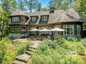 A large house with a stone foundation, multiple windows, and a patio with outdoor furniture.