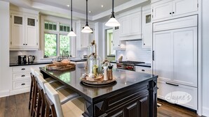 A spacious kitchen with white cabinets, a large island with stools, and pendant lighting. - Modern 5 bdrm, 5 bath cottage on Lake Rosseau! (Nipissing South (Utterson))