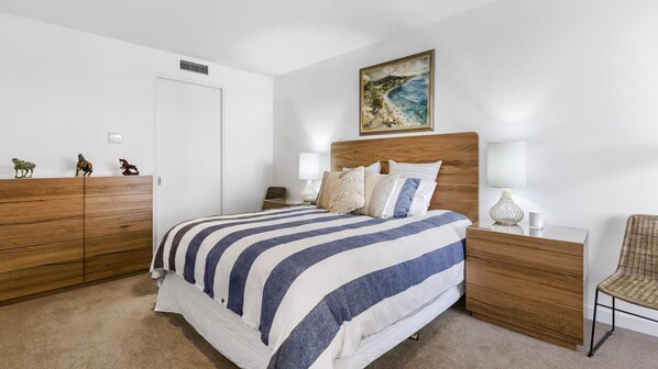 Quarto com uma cama grande, guarda-roupa de madeira e mesa de cabeceira com abajur.