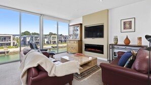 A modern living room with a fireplace, a TV, and a view of a water body and buildings.