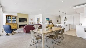 A modern living room with a fireplace, a dining area with a large table and chairs, and a kitchen with white cabinets and a sink. - MARINA VIEW Mornington (SAFETY BEACH)