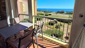 A balcony with a table and chairs, a view of the sea, and a well-maintained garden. - MAGNIFIQUE APPARTEMENT AVEC VUE IMPRENABLE SUR LA MER (LE CAP D AGDE)