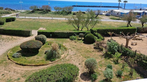 A landscaped garden with pathways, neatly trimmed hedges, and a view of the sea. - MAGNIFIQUE APPARTEMENT AVEC VUE IMPRENABLE SUR LA MER (LE CAP D AGDE)