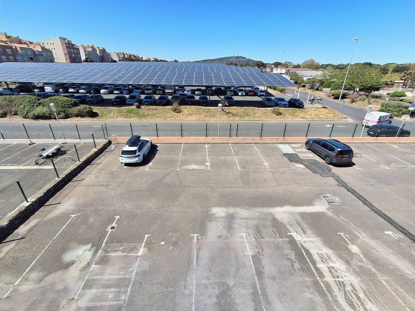 Un parking avec des panneaux solaires en arrière-plan, un ciel dégagé et un paysage vallonné.