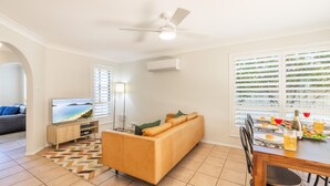 Uma sala de estar moderna com sofá, TV e área de jantar com mesa posta para uma refeição.