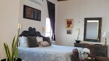 Un dormitorio con una cama, un aparador, una silla, una planta en maceta y un ventilador de techo.