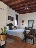 Un dormitorio con una cama, un aparador, una silla, una planta en maceta y un ventilador de techo.