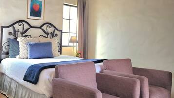 Une chambre à coucher avec un lit, une tête de lit, une fenêtre avec des rideaux, une lampe de chevet, un tableau encadré au mur et un tapis à motifs.