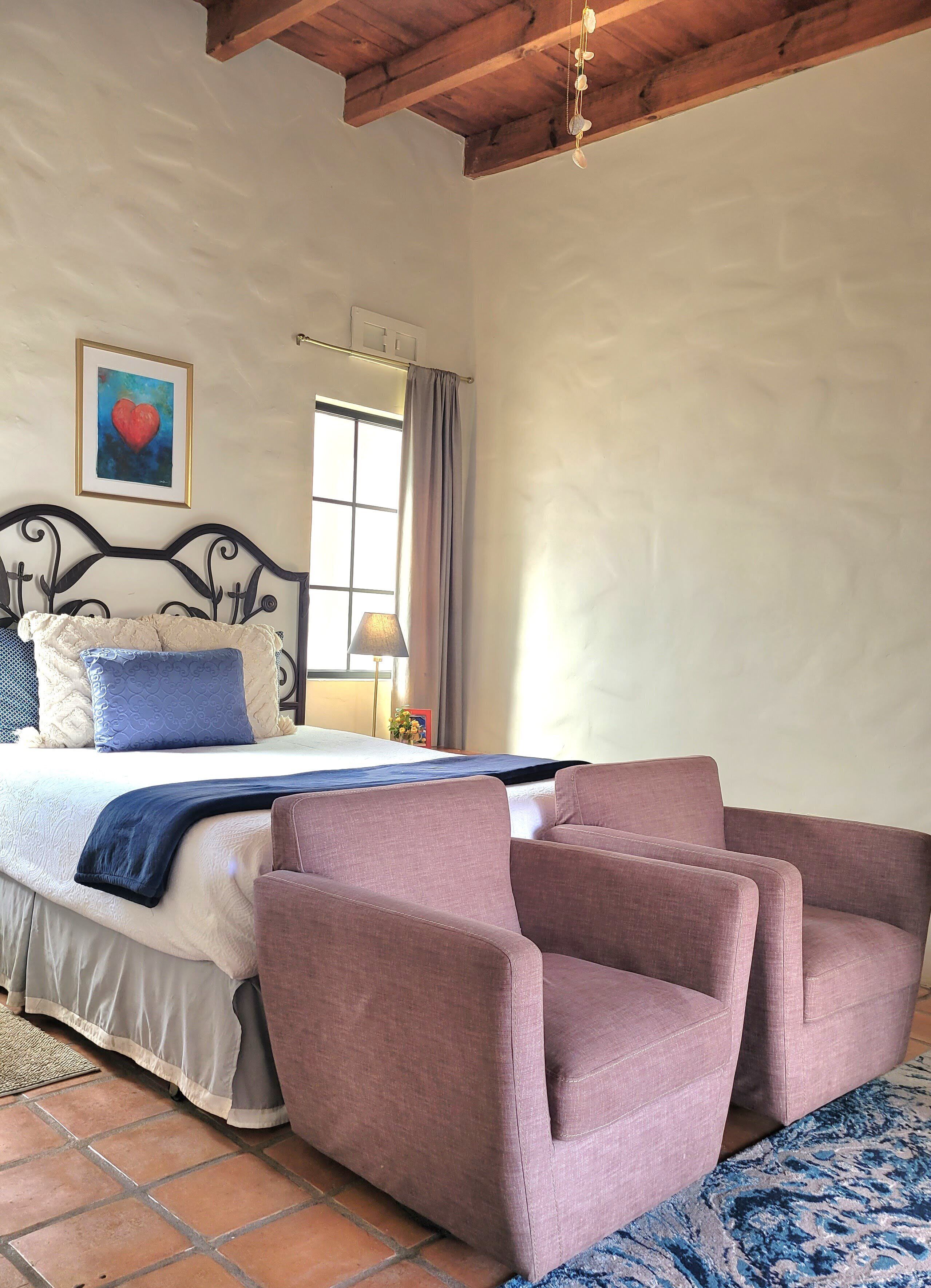 Quarto com cama, cabeceira, mesa de cabeceira com luminária, janela com cortinas e um quadro na parede.
