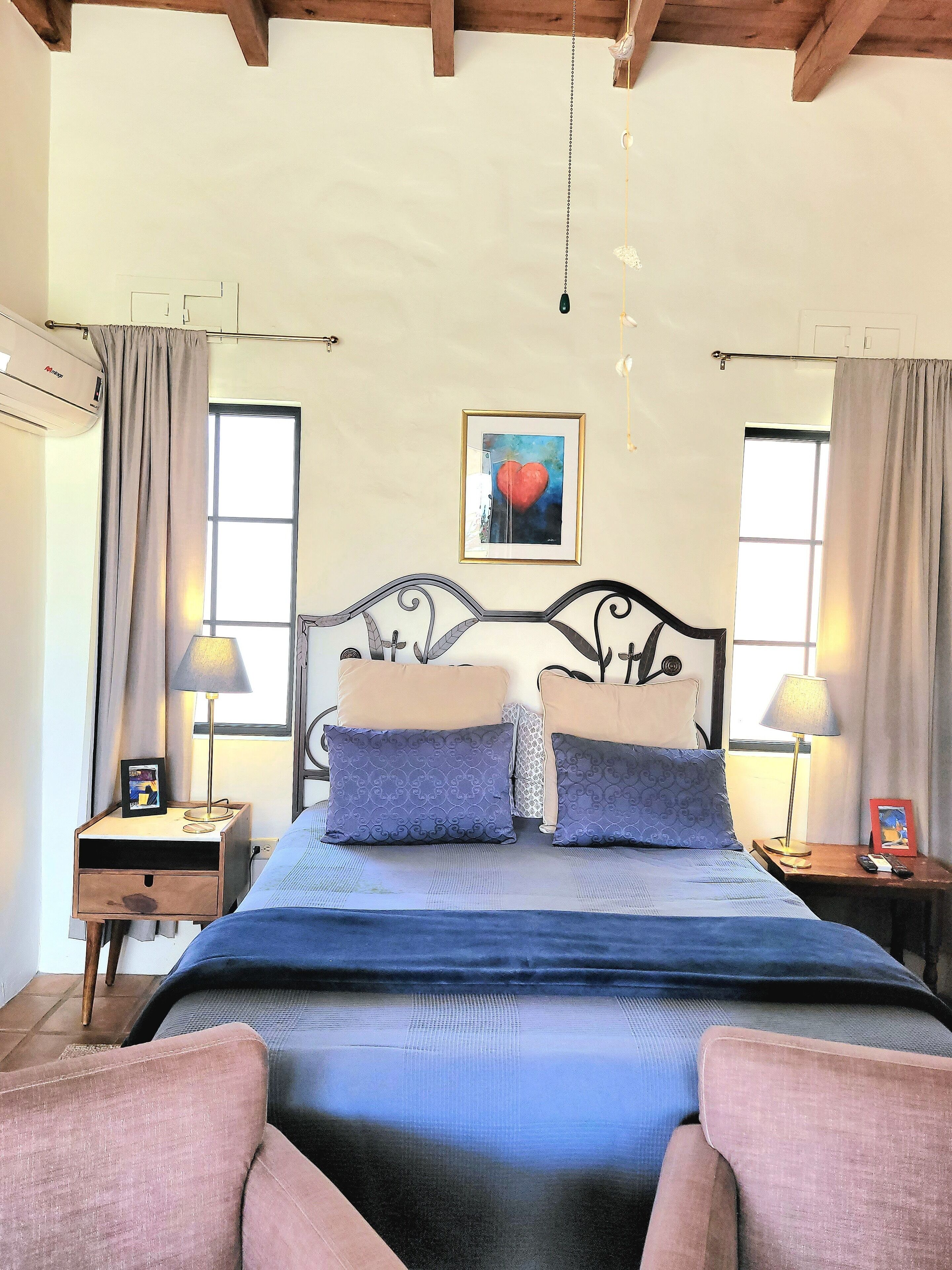 Una camera da letto con un letto, due comodini, una lampada a sospensione, un quadro appeso al muro e una finestra con tende.