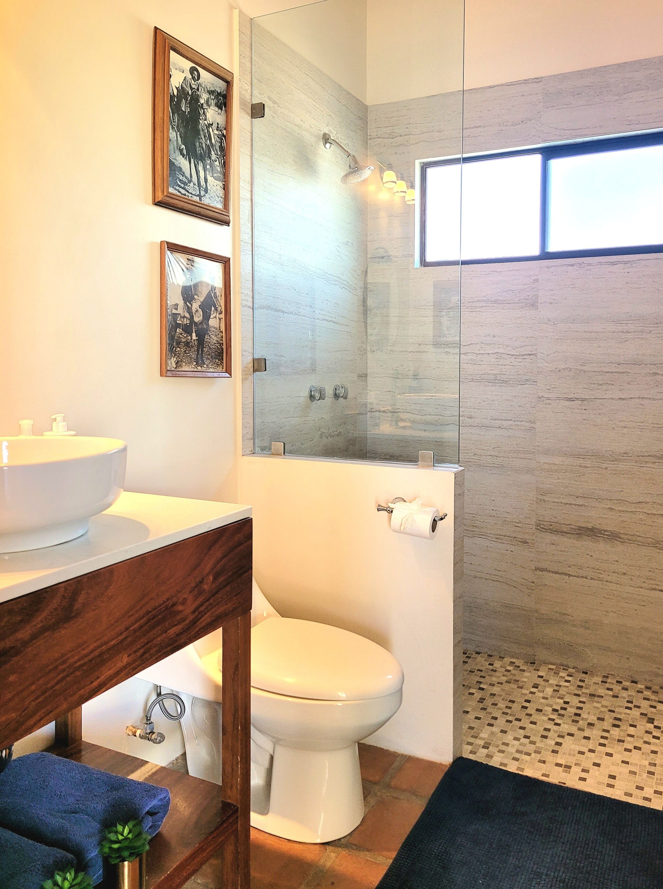 Un baño con inodoro blanco, lavamanos, espejo y zona de ducha.