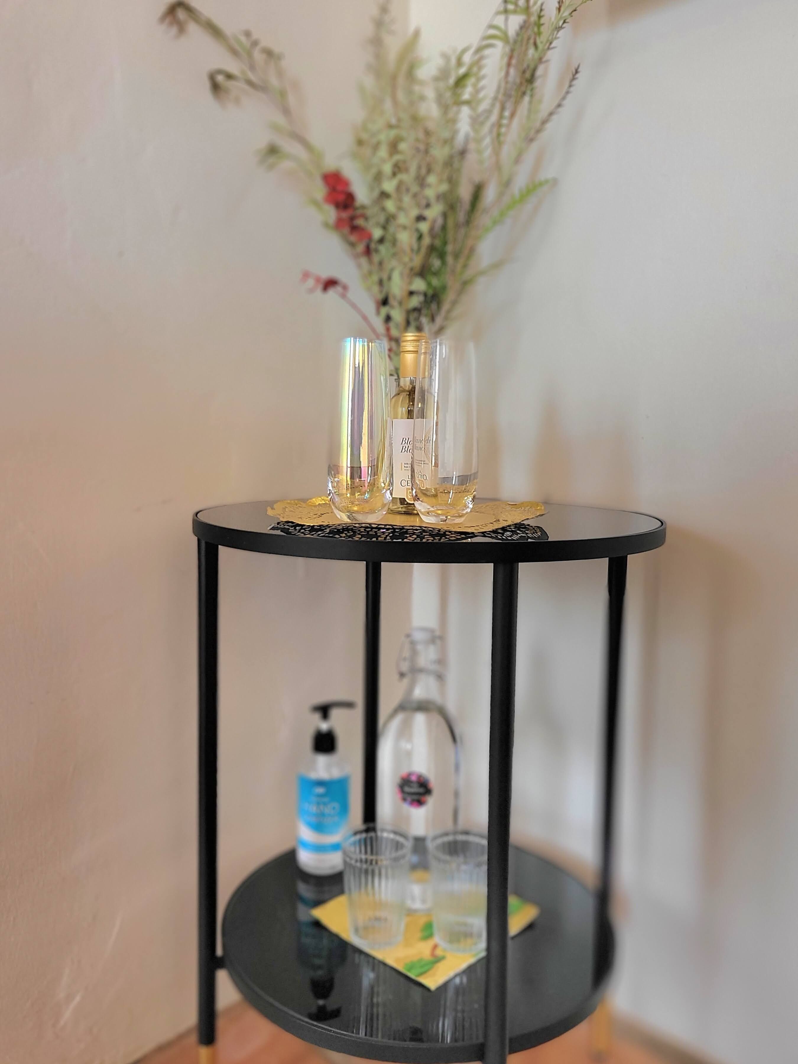 Uma pequena mesa preta com duas garrafas de vidro transparente e um vaso com flores secas.