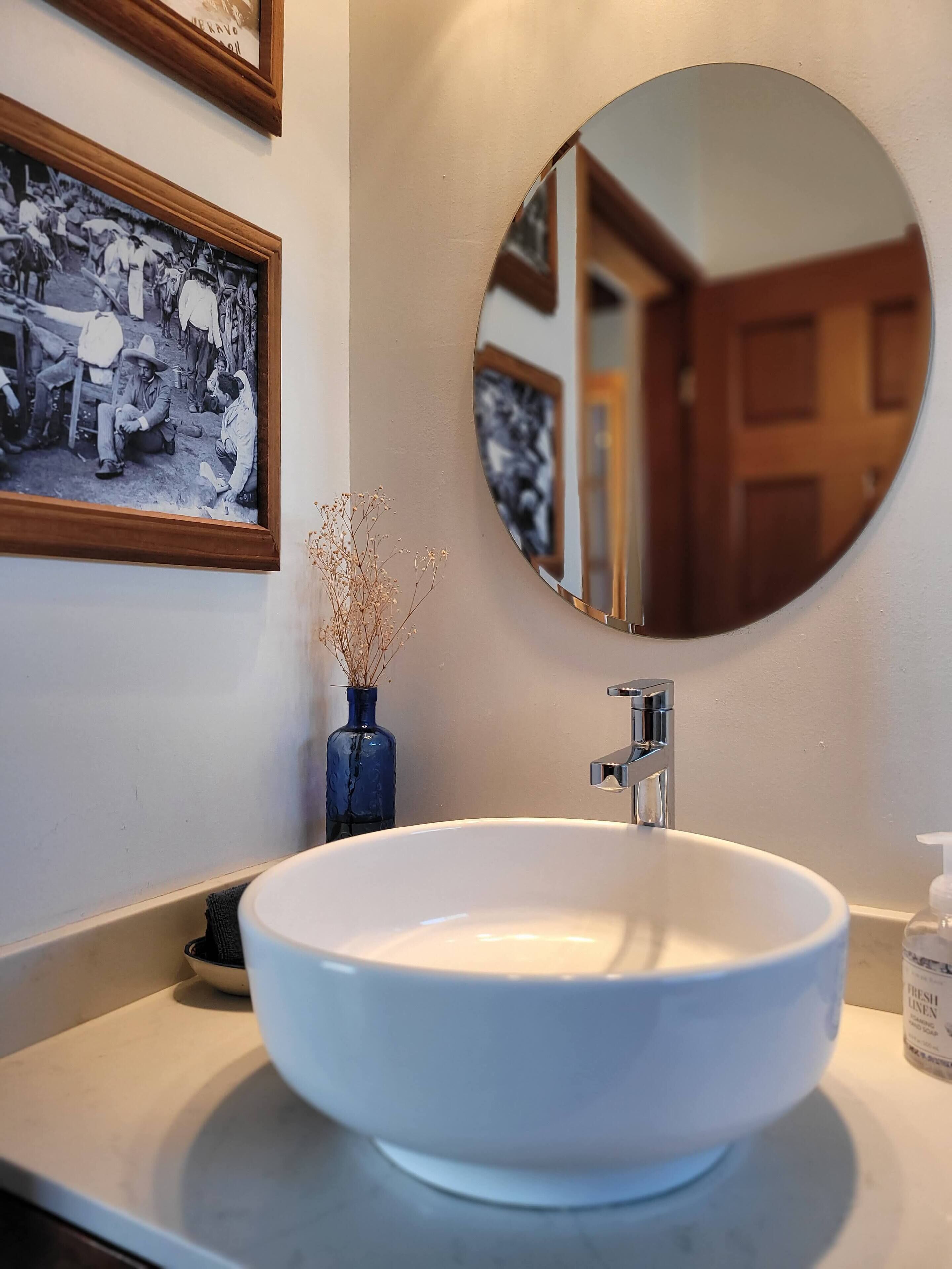 Un baño con un lavamanos blanco, un espejo redondo y una fotografía en blanco y negro enmarcada en la pared.