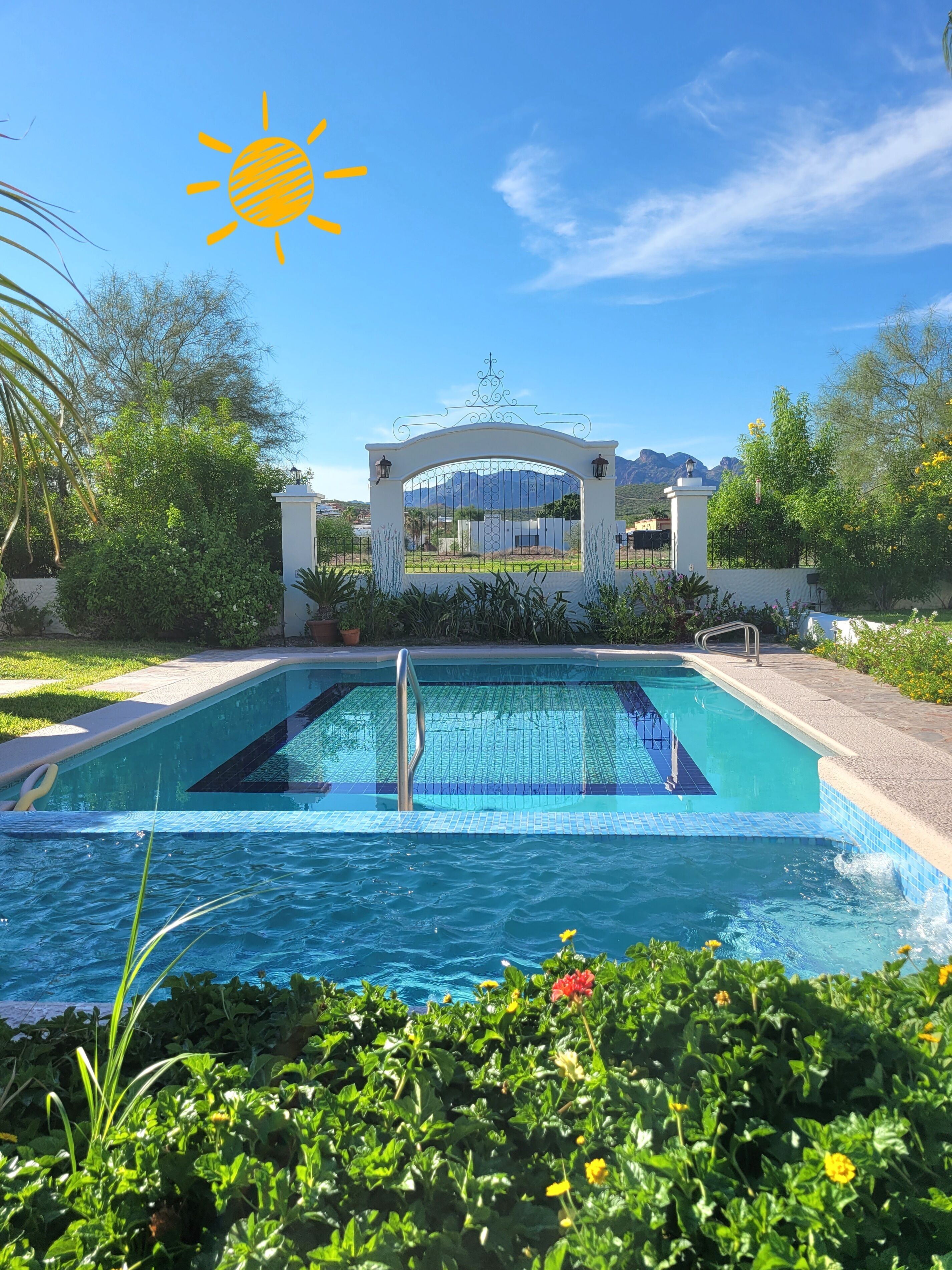 Piscina com vista para montanhas ao fundo, rodeada por vegetação e um portão branco.
