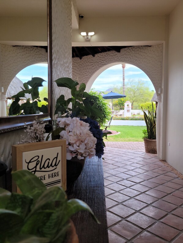 Ein überdachter Patio-Bereich mit Fliesenboden, Pflanzkübeln und einem Schild mit der Aufschrift 'Glad You're Here'.