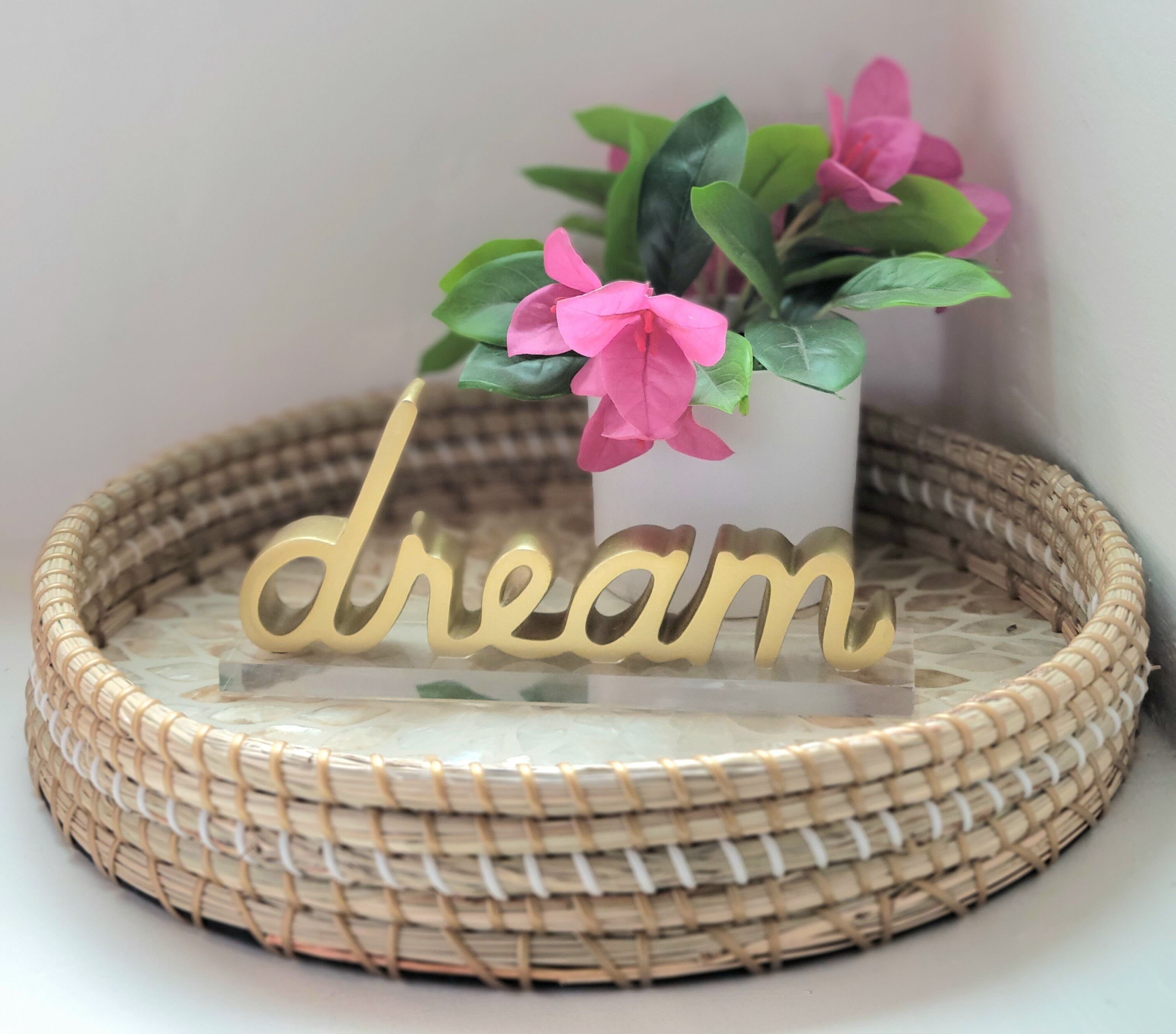 Un plateau en osier orné du mot décoratif « rêve » et une petite plante en pot aux fleurs roses.