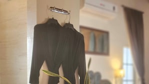 A hotel room with a bed, a bedside table with rolled towels, a potted plant, and a black outfit hanging on a wall-mounted rack. - Casa Magdalena B&B (San Carlos)