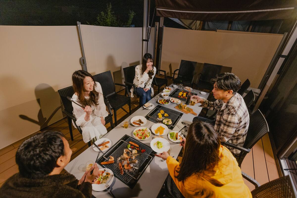 A group of people dining outdoors at a table with various dishes, including grilled food and salads.