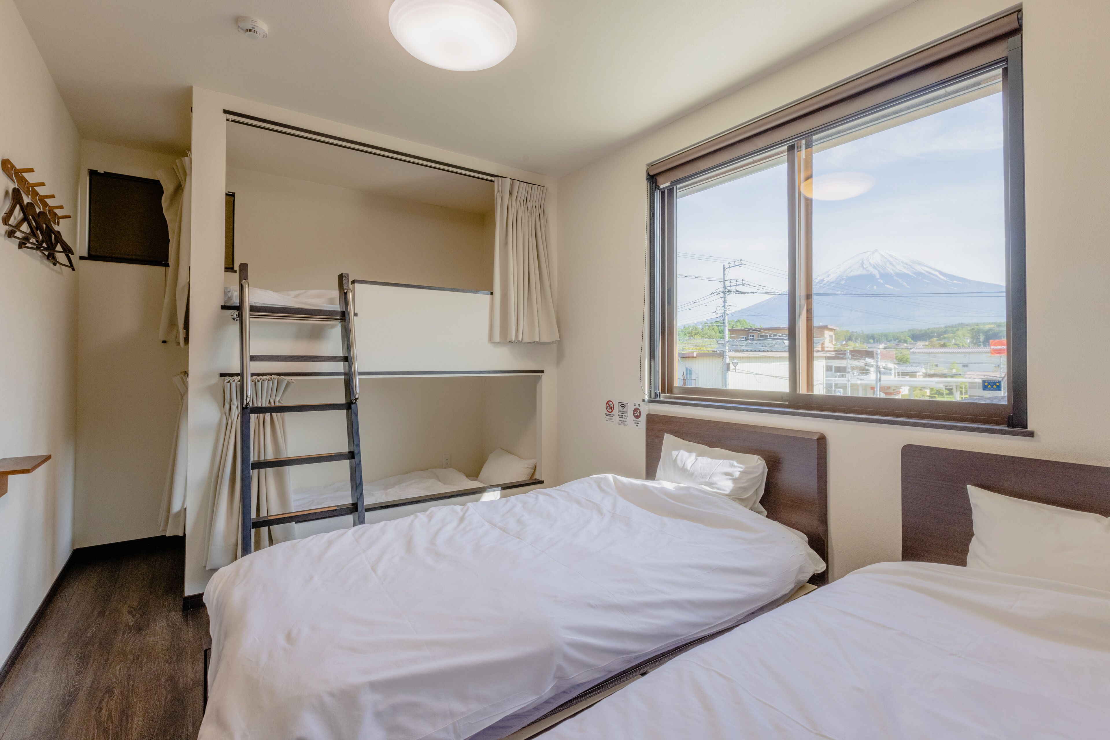 A hotel room with two beds, a bunk bed, a window with a view of a mountain, and a wooden floor.