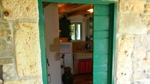 Habitación con paredes de piedra y una puerta verde que da a una cocina.