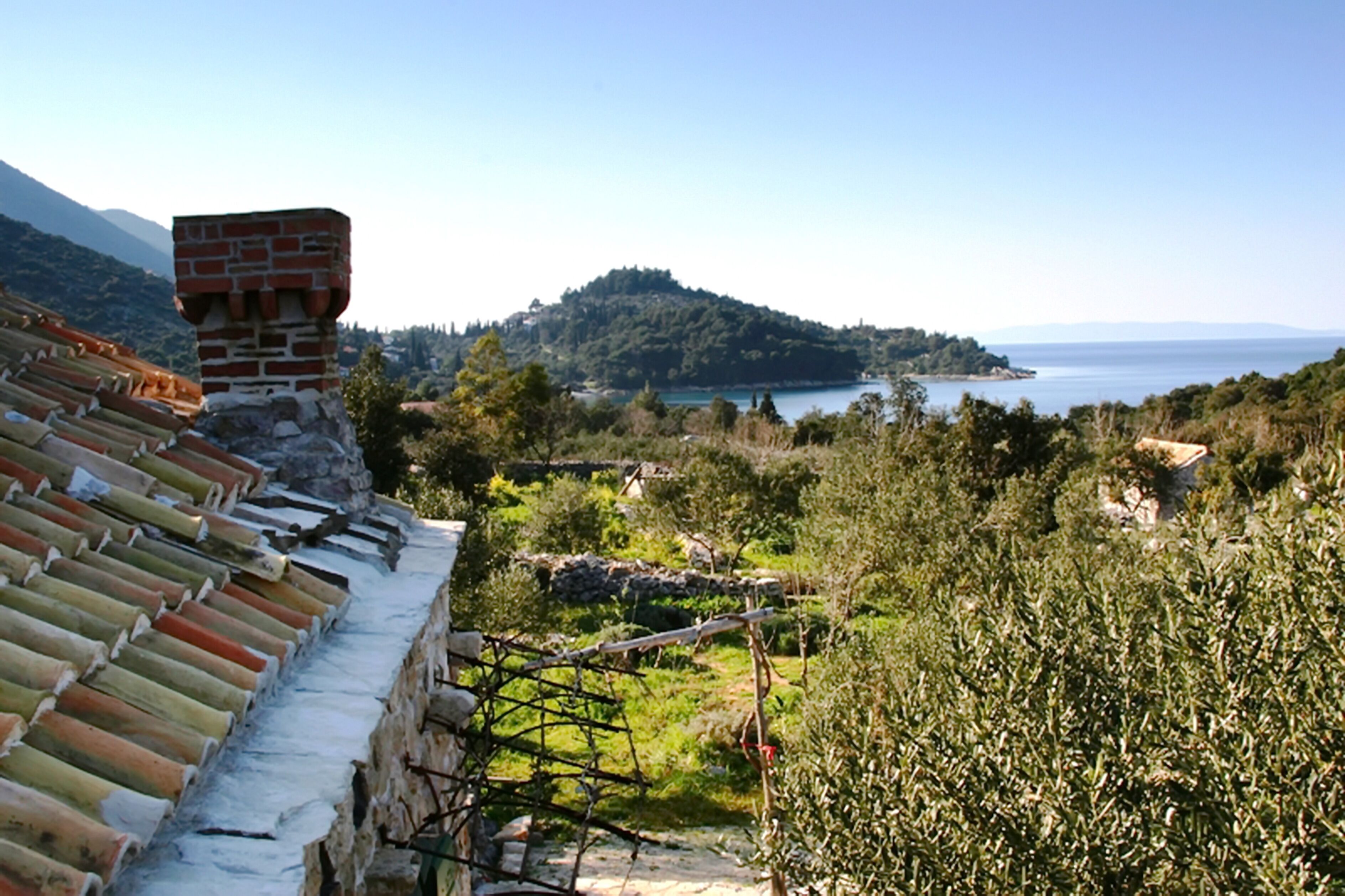 Une vue sur la côte, avec un mur de pierre et un toit en tuiles, un paysage verdoyant luxuriant et une colline au loin.