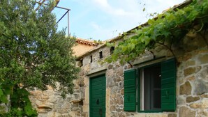 Edificio de piedra con dos puertas verdes y ventanas, rodeado de vegetación y plantas de lavanda.