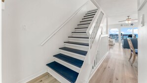 Un escalier avec des rampes blanches et des marches sombres menant à un balcon d’où l’on peut admirer l’océan.