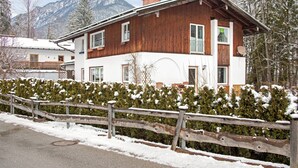 Ein zweistöckiges Holzhaus mit weißer Fassade, einem Balkon und Blick auf schneebedeckte Berge.