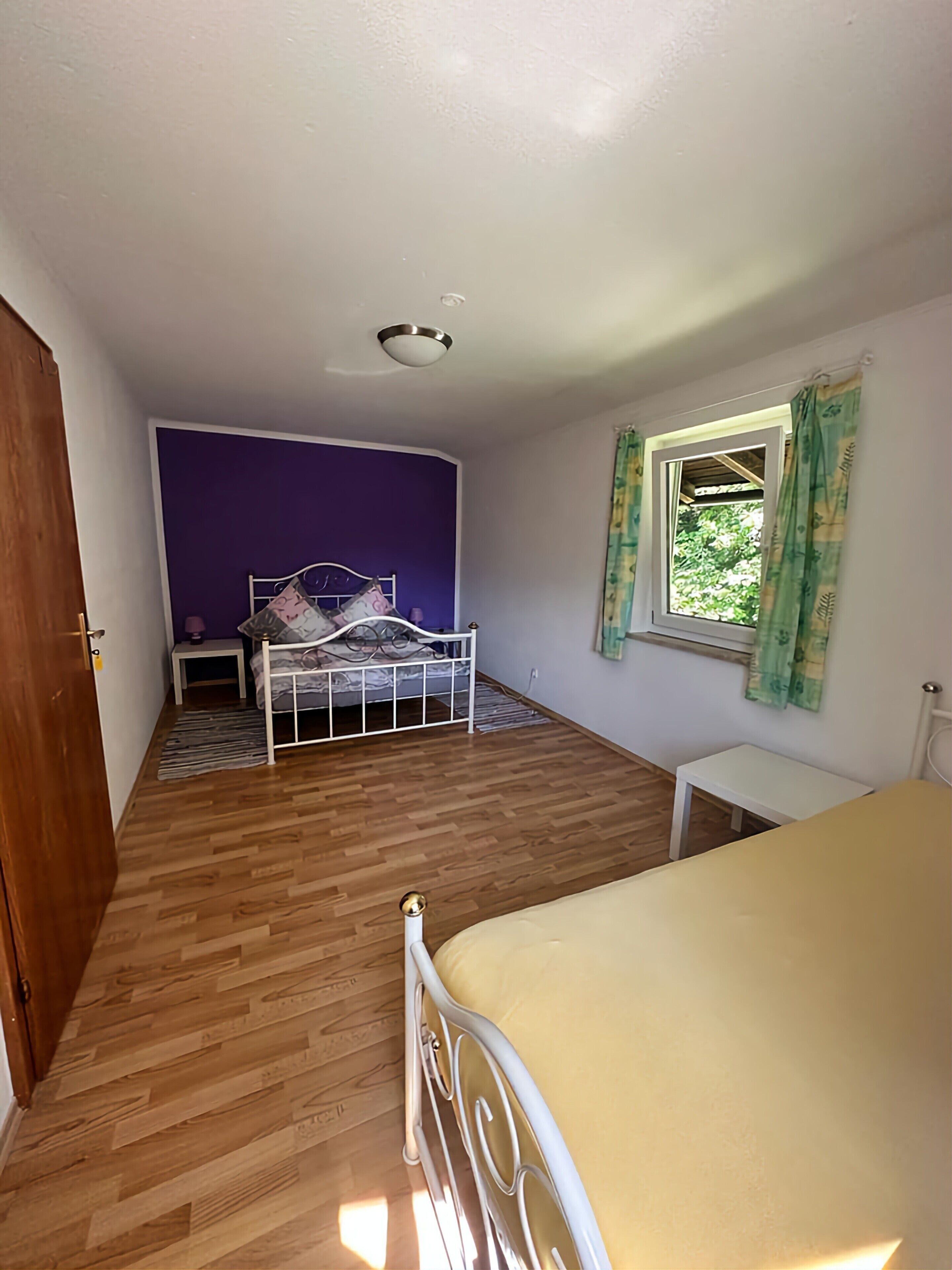 Ein Schlafzimmer mit Bett, einem fenster mit Vorhängen, einem Nachttisch und Holzboden.
