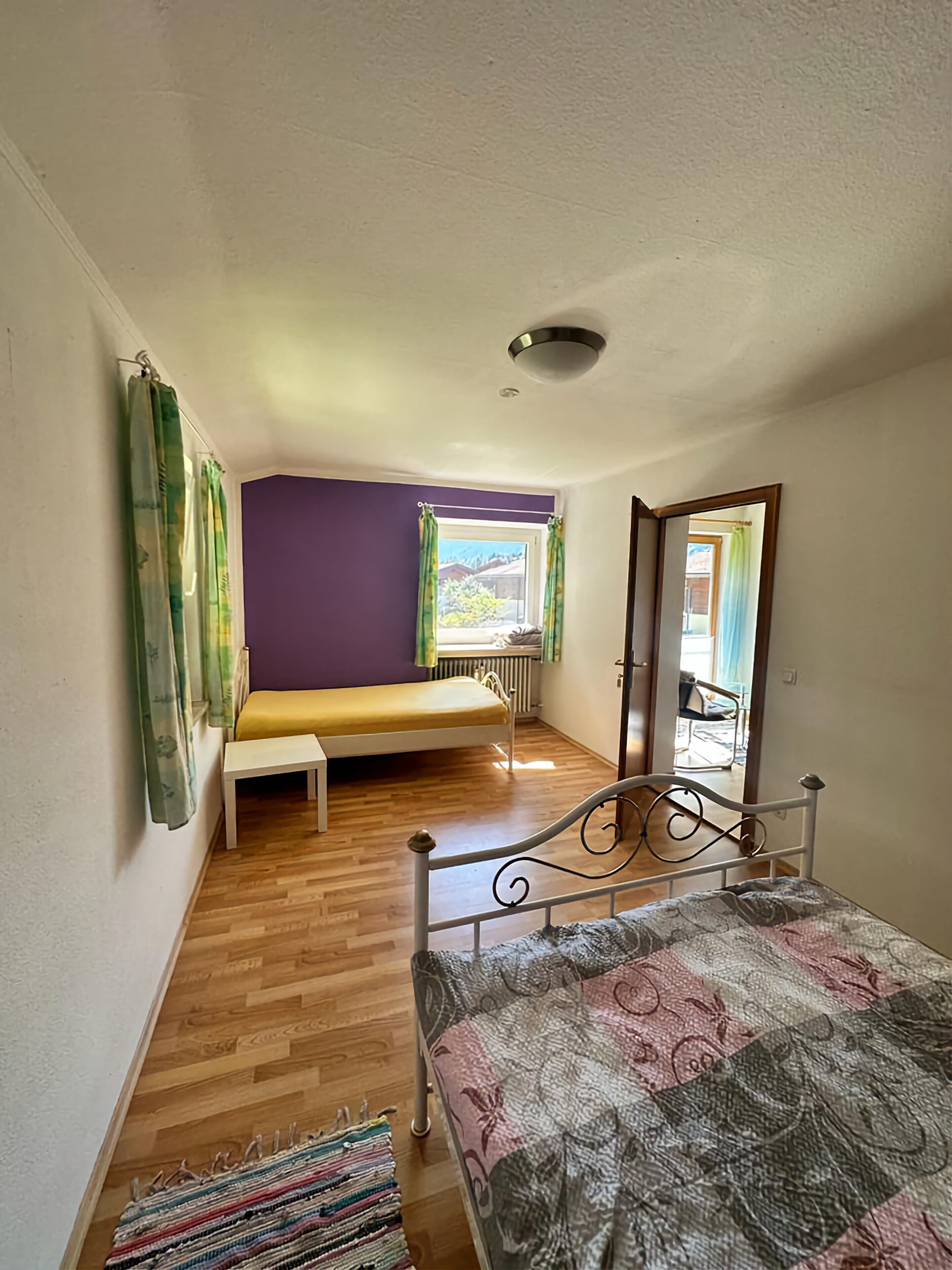 A room with a bed, a bench, a window with curtains, and a radiator.