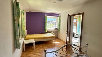 A room with a bed, a bench, a window with curtains, and a radiator.