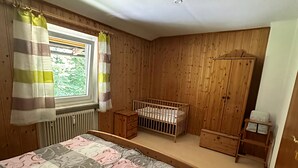 Ein Schlafzimmer mit einem Bett, einem Babybett, einem Holzschrank und einem Fenster mit Vorhängen.