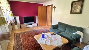 Ein Wohnzimmer mit einem grünen Sofa, einem Holztisch, einem Fernseher und einem roten Teppich mit Muster.