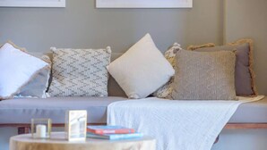 A cozy living room with a grey sofa, patterned cushions, and a small wooden side table with books and a candle. - Lovely in the Heart of Town steps from everything (Tamarindo)