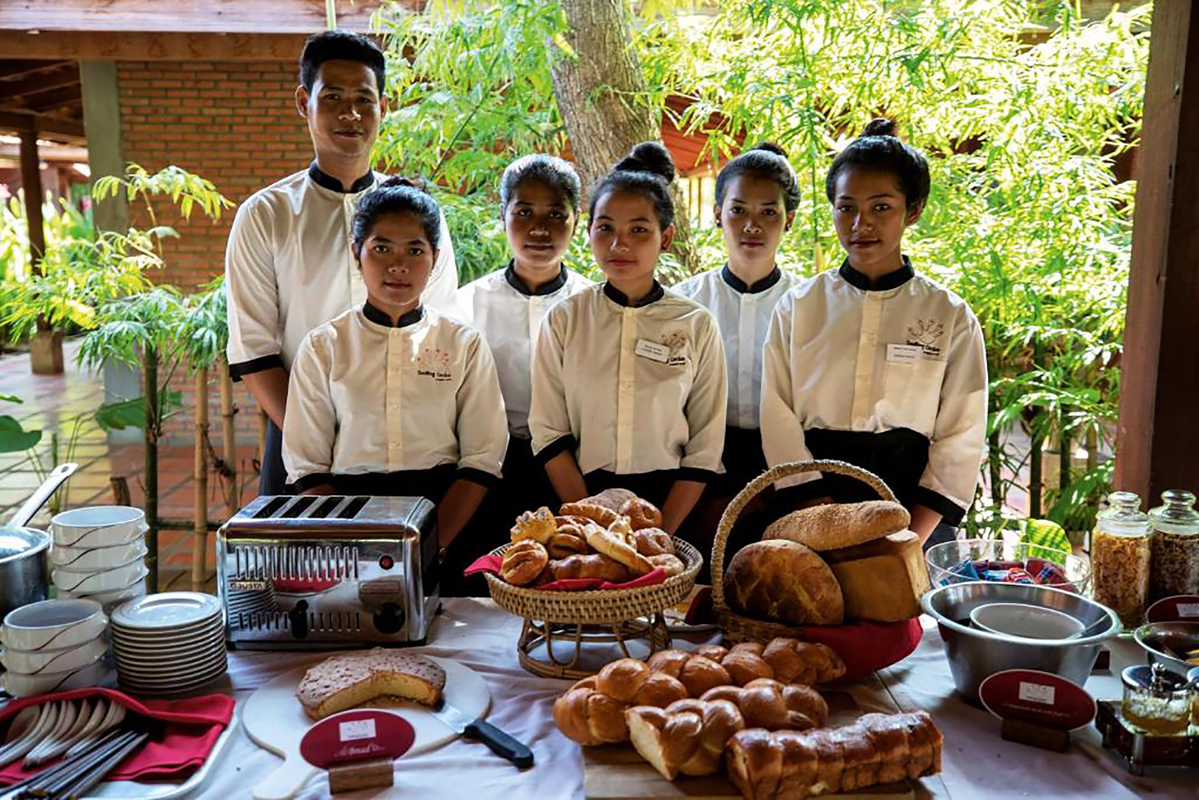 A group of people in chef uniforms standing behind a table with various baked goods and kitchen equipment.