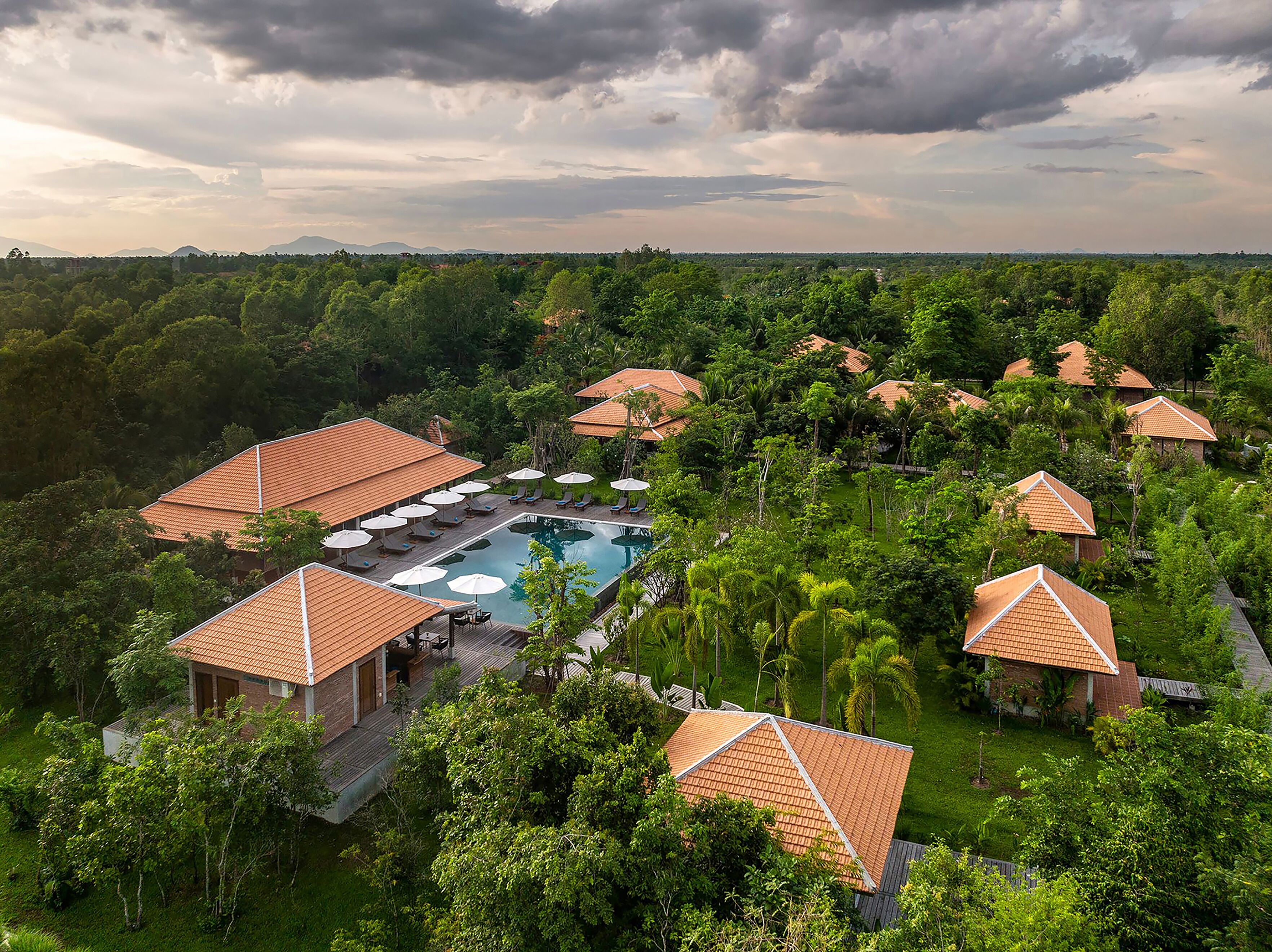 A resort with multiple bungalow-style buildings, a central swimming pool, and lush greenery surrounding the property.